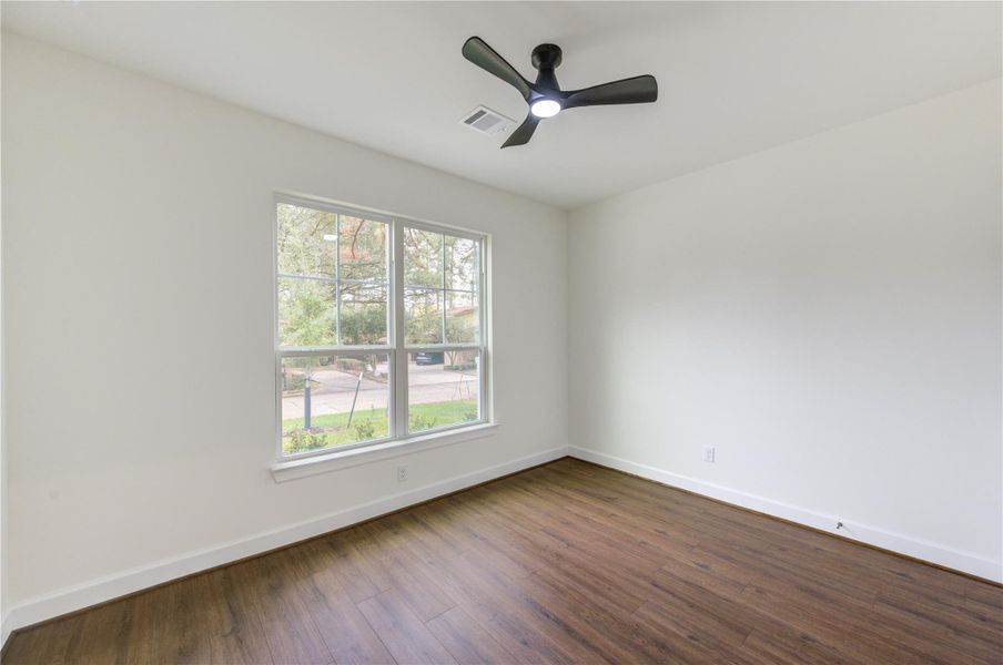 This is a bright, secondary bed room with clean white walls and luxury vinyl wood flooring. It features a modern ceiling fan and a simple door leading to another area.
