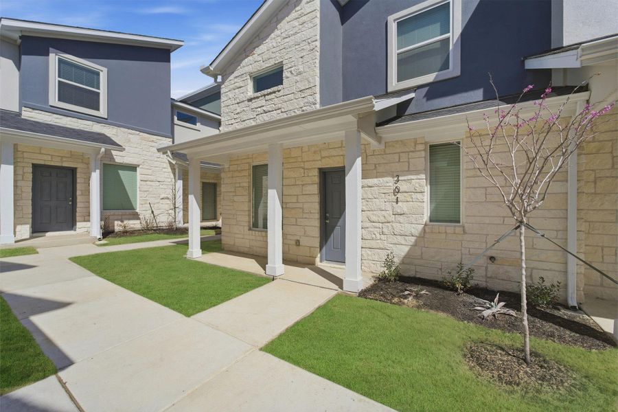 Doorway to property with stone siding, stucco siding, a lawn, and a porch