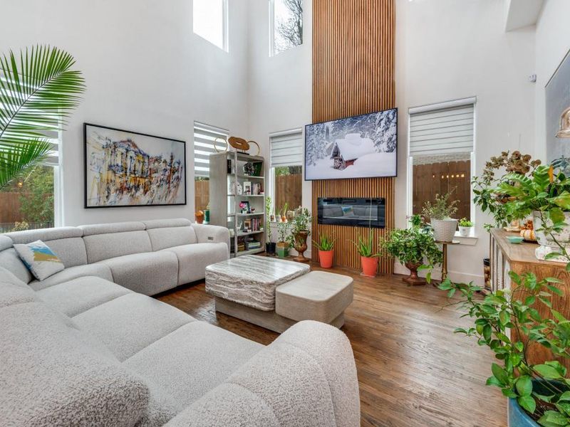 Living area with a towering ceiling, wood finished floors, and a glass covered fireplace