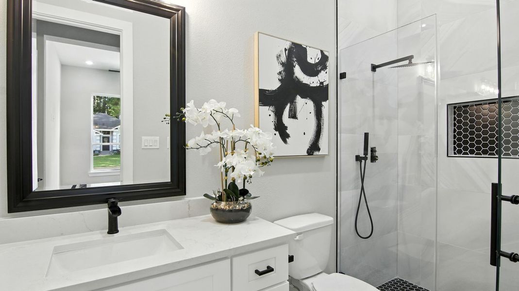 This beautifully designed full bathroom combines sophistication and functionality with its sleek white vanity, quartz countertop, and matte black fixtures. The glass-enclosed shower features striking tilework with hexagonal accents and a built-in niche, adding both style and practicality This beautifully designed full bathroom combines sophistication and functionality with its sleek white vanity, quartz countertop, and matte black fixtures. The glass-enclosed shower features striking tilework with hexagonal accents and a built-in niche, adding both style and practicality