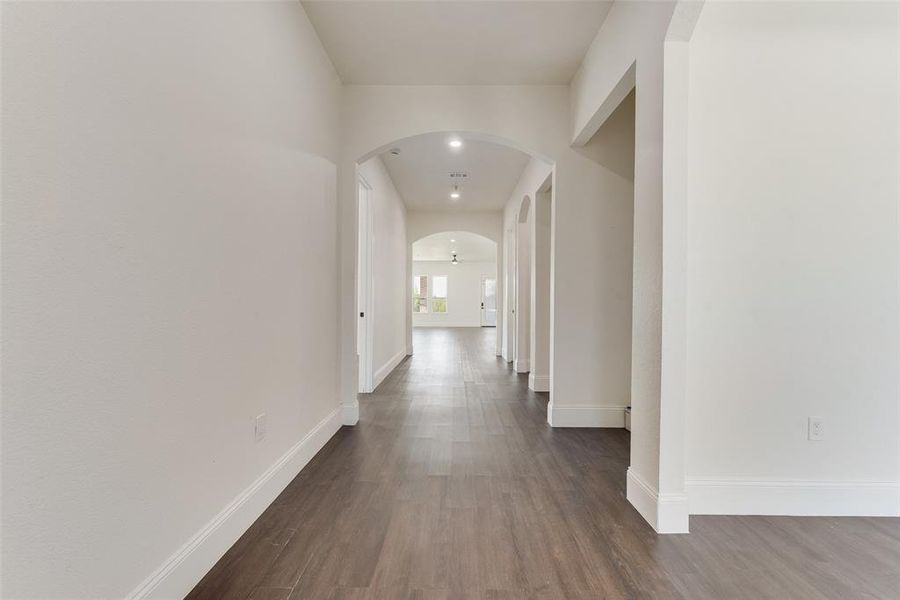 Long hallway with dark wood-finish flooring, white walls, and multiple arched doorways Long hallway with dark wood-finish flooring, white walls, and multiple arched doorways