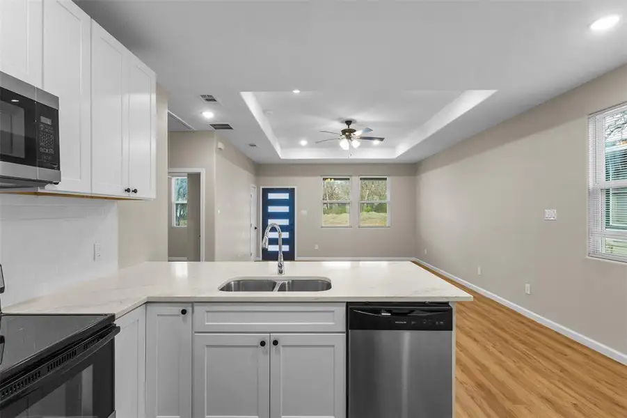 Kitchen with stainless steel appliances, a peninsula, a tray ceiling, white cabinetry, and light stone counters