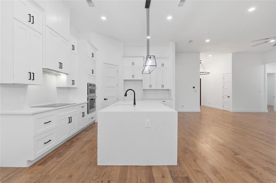 Kitchen featuring light stone countertops, white cabinetry, a kitchen island with sink, light wood-style flooring, and open floor plan