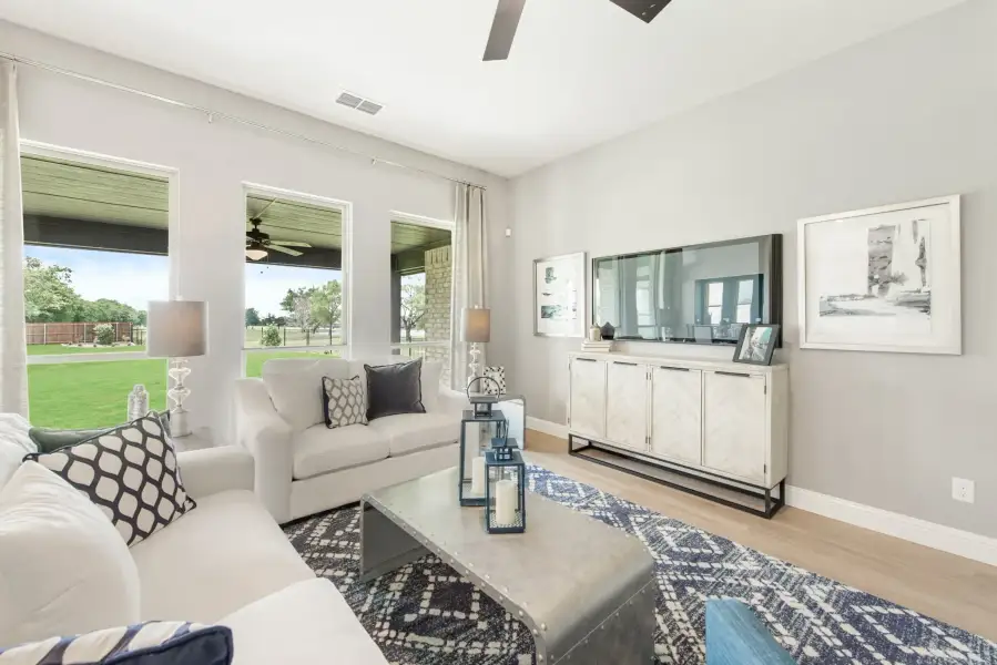 Living room with white sofas, large windows, ceiling fan, and TV on a white sideboard with hardwood floors