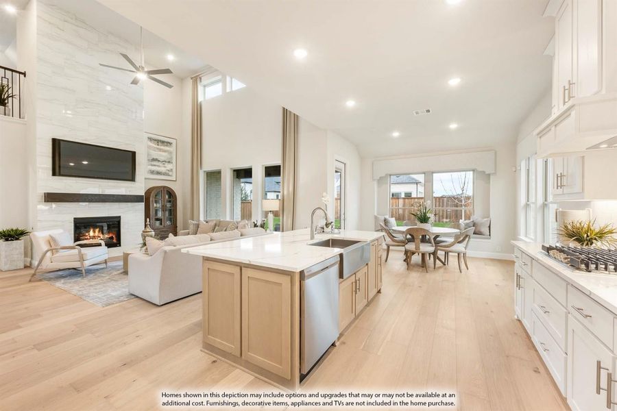 Open-concept kitchen and living area with large island, stone fireplace, high ceilings, and light hardwood floors
