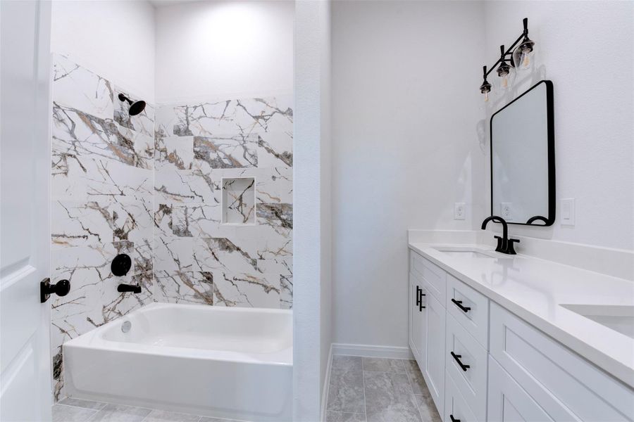 Secondary bath featuring a striking marble-look tile surround with bold veining, paired with matte black shower fixtures. Double vanity with white shaker cabinetry, quartz countertop, and framed mirrors adds both style and functionality, finished with modern vanity lighting above.