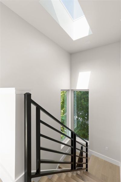 A modern staircase features light hardwood steps beneath a large overhead skylight.