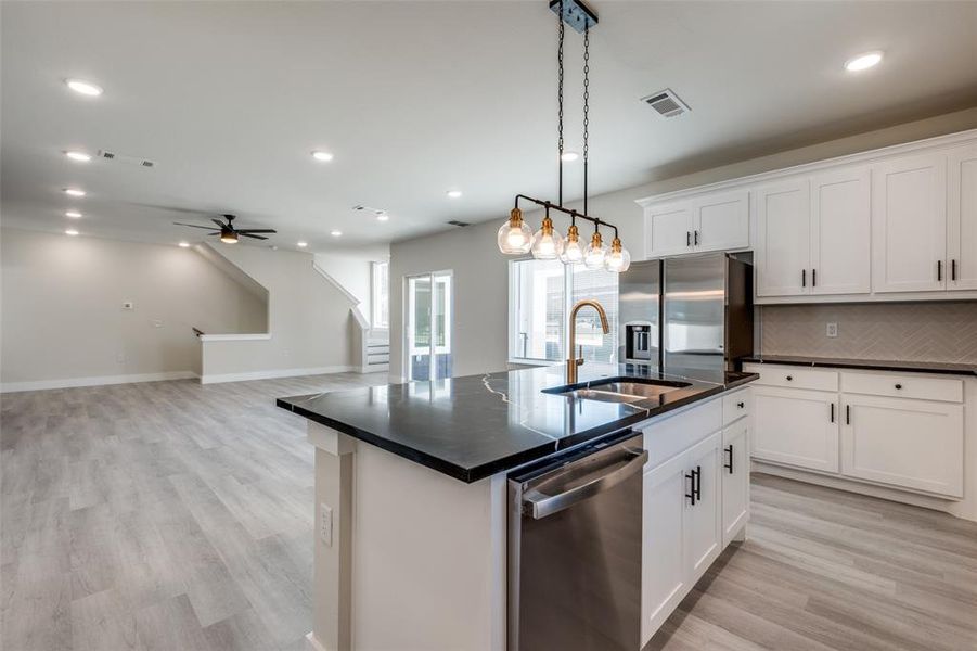 Kitchen with stainless steel appliances, a kitchen island with sink, hanging light fixtures, white cabinetry, and light wood-type flooring