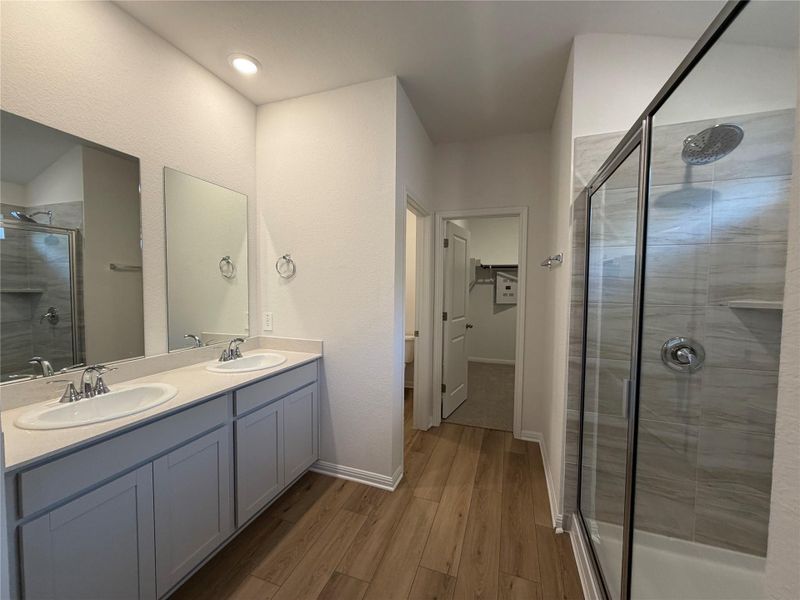 Full bathroom featuring a shower stall, a spacious closet, double vanity, and dark wood-style flooring