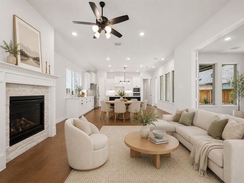Open-concept living space featuring hardwood flooring, a fireplace with a white mantel and stone surround, recessed lighting, and multiple windows