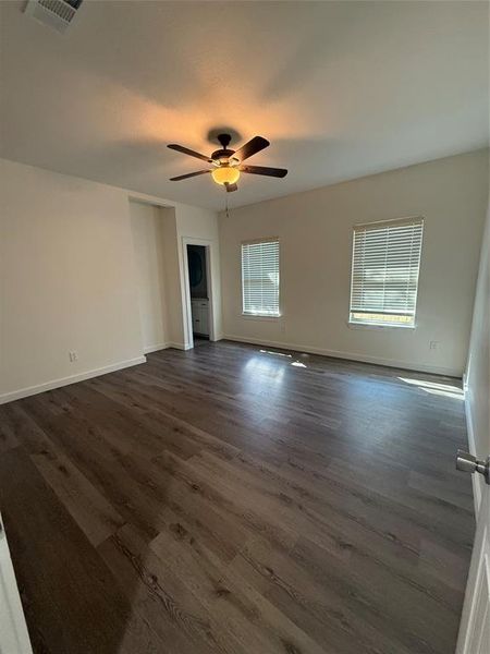 Unfurnished room featuring dark wood-type flooring, visible vents, ceiling fan, and baseboards