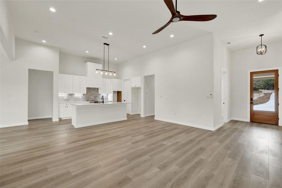 Unfurnished living room featuring a towering ceiling, light wood finished floors, a chandelier, recessed lighting, and ceiling fan