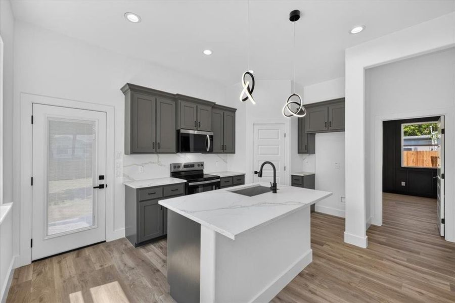Modern kitchen featuring an island with an undermount sink and matte black faucet, dark gray cabinetry, white countertops with veining, and wood-finish flooring Modern kitchen featuring an island with an undermount sink and matte black faucet, dark gray cabinetry, white countertops with veining, and wood-finish flooring