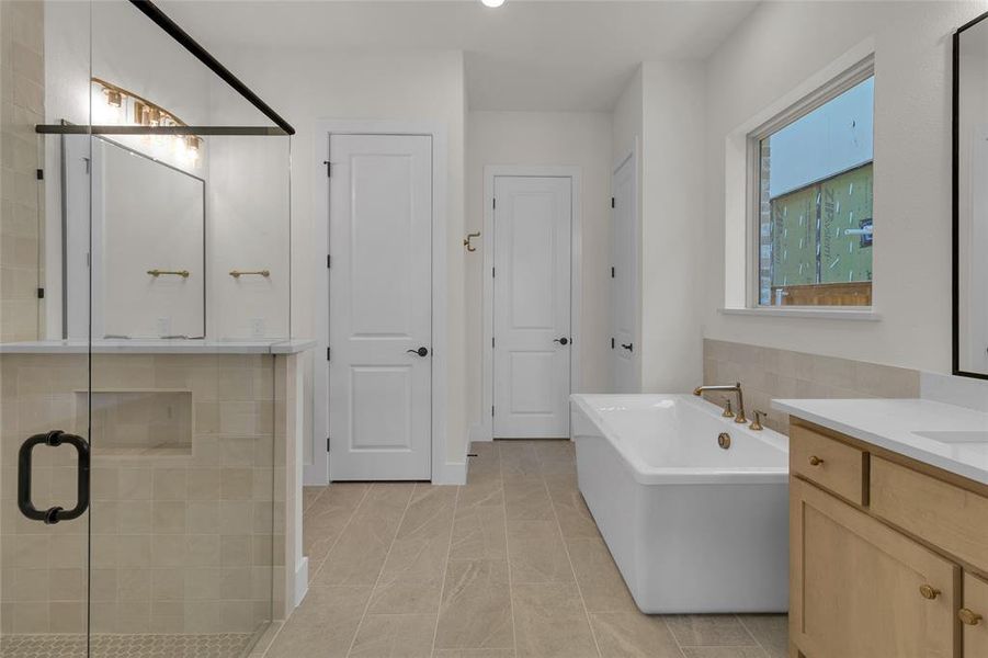 Spacious bathroom featuring a freestanding soaking tub, a large walk-in shower with clear glass enclosure, and a vanity with a light wood-finish cabinet and white countertop