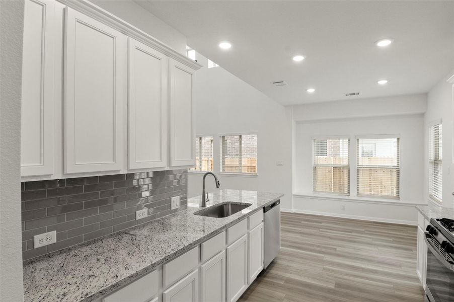 Kitchen featuring range with gas cooktop, light wood-style flooring, white cabinets, tasteful backsplash, and light stone countertops Kitchen featuring range with gas cooktop, light wood-style flooring, white cabinets, tasteful backsplash, and light stone countertops