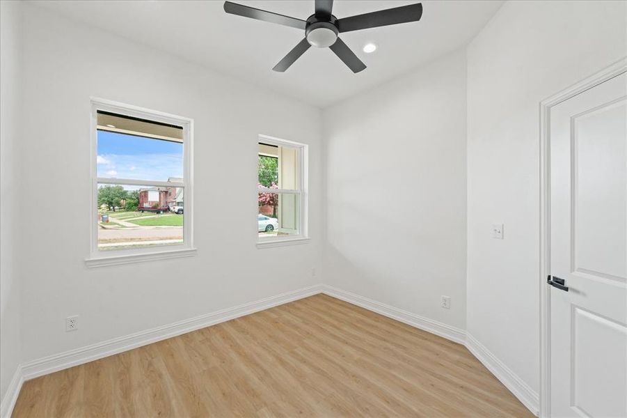 Bright room featuring two windows, wood-finish flooring, white baseboards, and a black ceiling fan with an integrated light