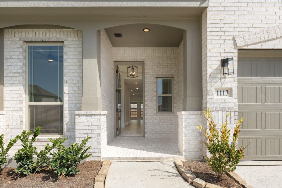 Home entryway with white brick exterior, arched covered porch, open front door, and attached garage
