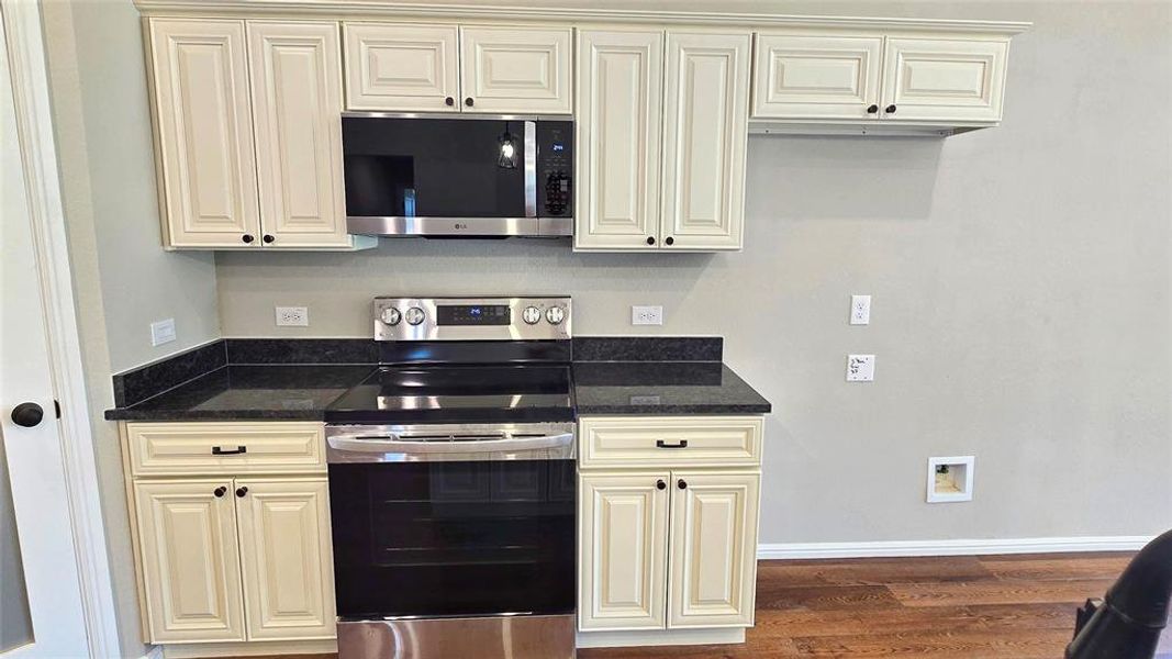 Kitchen with stainless steel appliances, cream cabinets, and wood finished floors
