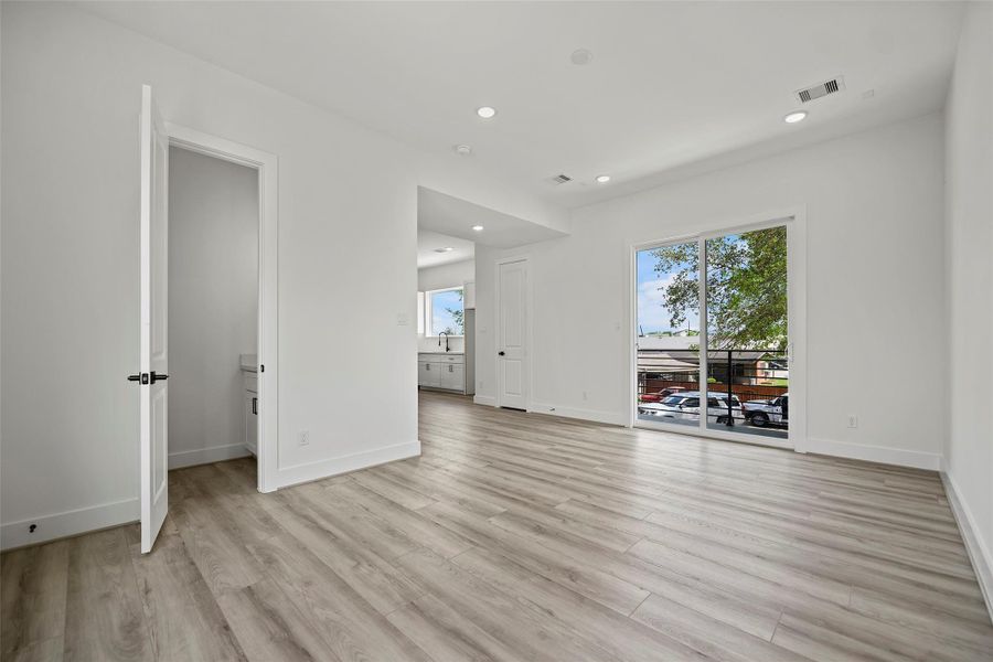 Living area has modern features, sleek LVP flooring, a large sliding glass door leading to a balcony, and a view of the neighboring area. It includes a doorway to a half bathroom and an open connection to the kitchen area.