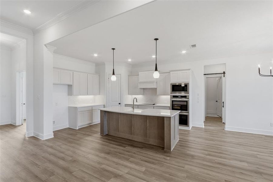 Kitchen with a barn door, a kitchen island with sink, ornamental molding, stainless steel appliances, and light stone counters