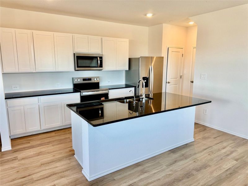 Kitchen with white cabinetry, stainless steel appliances, an island with sink, light wood-style floors, and recessed lighting