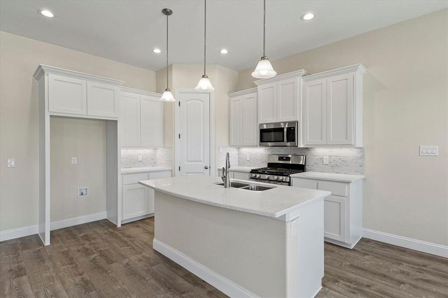 Kitchen with appliances with stainless steel finishes, a center island with sink, tasteful backsplash, dark wood-type flooring, and white cabinets