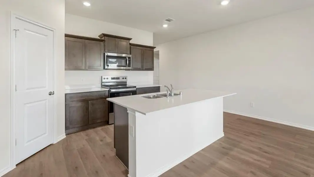 Open-concept kitchen featuring an island with a sink, stainless steel appliances, dark wood-finish cabinetry, white countertops, and wood-finish flooring