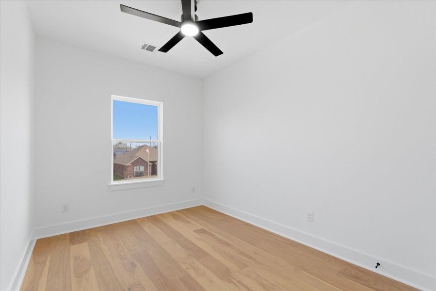 Second-floor bedroom with beautiful hardwood flooring and a sleek black ceiling fan enhancing the room’s modern appeal.
