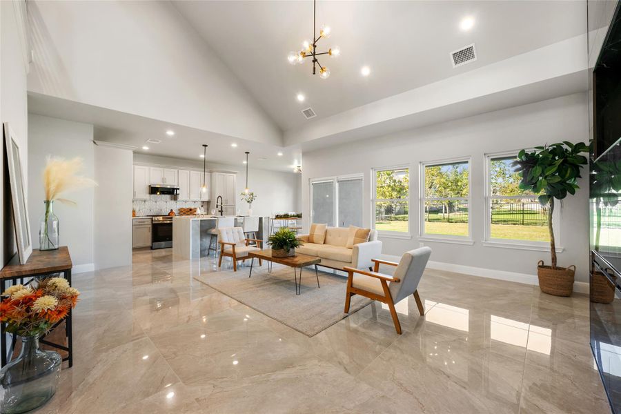 Living room featuring high vaulted ceiling, a chandelier, light marble finish flooring, and recessed lighting