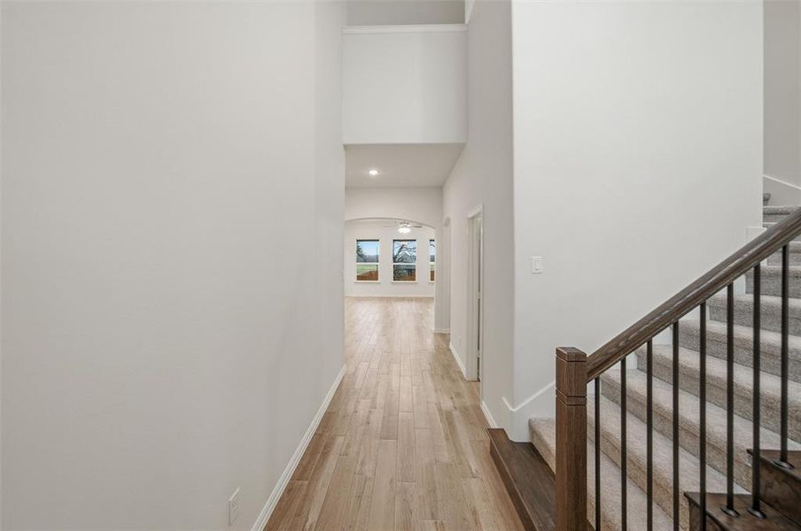 Hallway featuring light wood-style flooring, recessed lighting, a high ceiling, and arched walkways