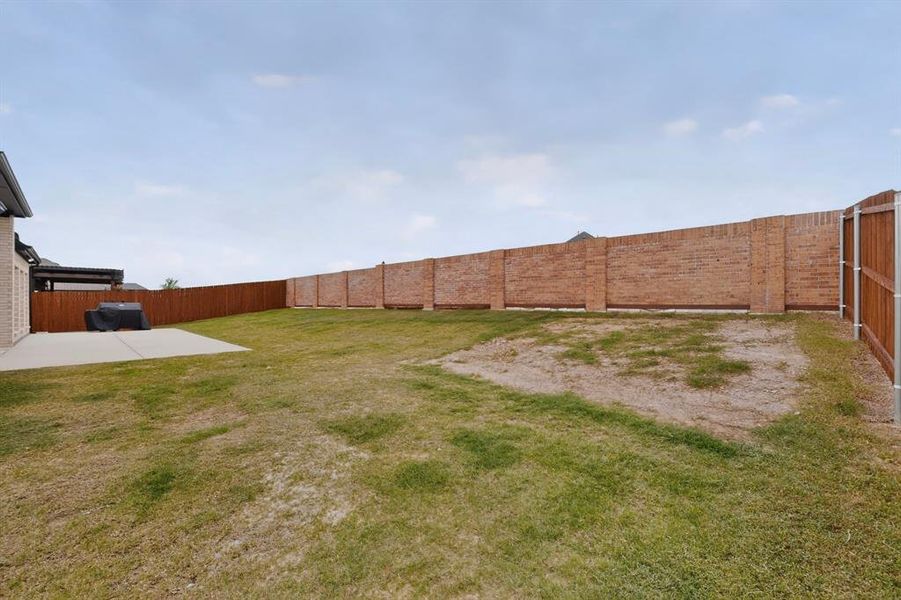 Expansive backyard featuring a concrete patio, brick exterior wall, and wood fencing Expansive backyard featuring a concrete patio, brick exterior wall, and wood fencing