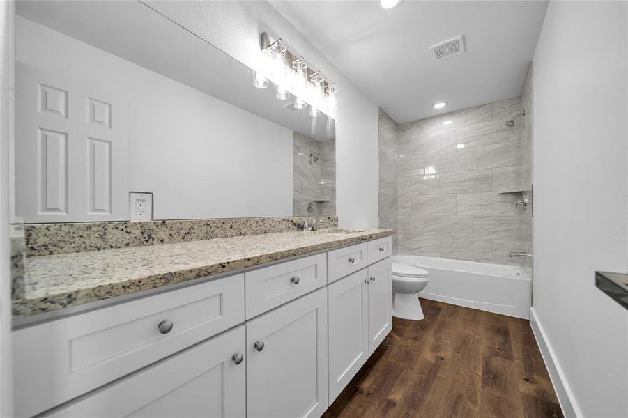 Full bath featuring vanity, visible vents, toilet, wood finished floors, and baseboards