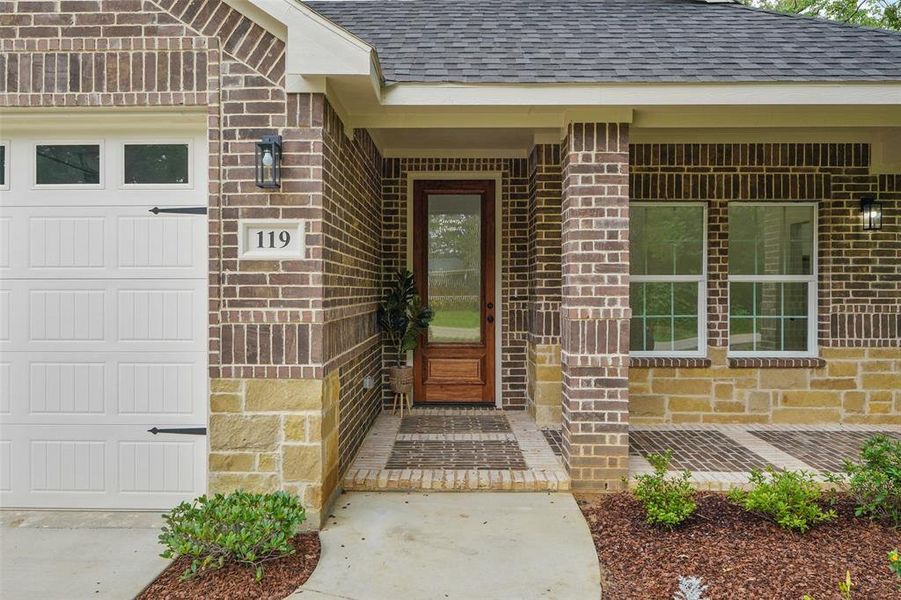 Brick and stone exterior with a white paneled garage door, a glass-paneled wooden entry door, and exterior sconce lighting Brick and stone exterior with a white paneled garage door, a glass-paneled wooden entry door, and exterior sconce lighting
