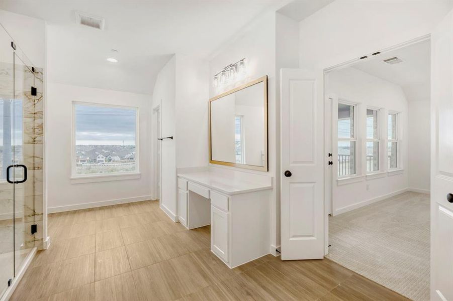 Spacious bathroom featuring a glass-enclosed shower with stone-look tile, wood-finish flooring, a vanity with a white countertop and built-in drawers, and a large window