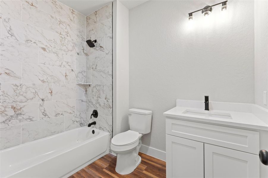 Bathroom with vanity, dark wood-style flooring,  shower combination, and a textured wall