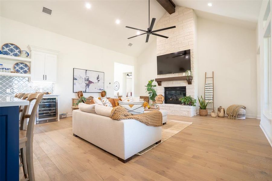 Living area with light wood finished floors, beverage cooler, vaulted ceiling, a stone fireplace, and a dry bar Living area with light wood finished floors, beverage cooler, vaulted ceiling, a stone fireplace, and a dry bar