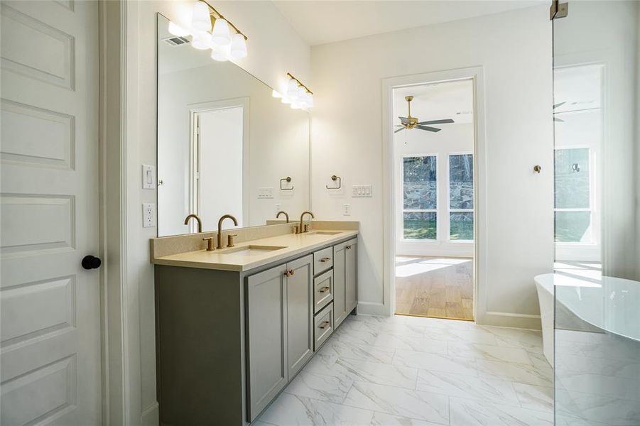 Full bath featuring light marble finish floors, double vanity, a soaking tub, and a ceiling fan