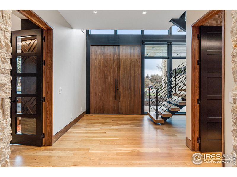 A grand entry with custom solid walnut pivot door (with Emtek hardware).  The door to the right is a walk-in entry closet with built-in Shiloh Cabinets, a Pental Quartz slab bench and Black Edition Wallpaper.