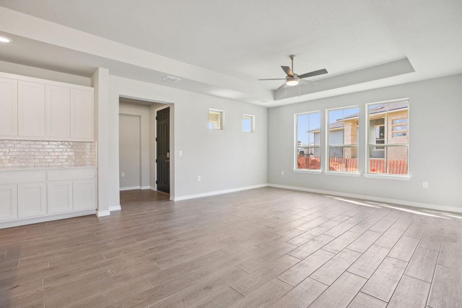 Unfurnished living room featuring a tray ceiling, light wood-style floors, and ceiling fan