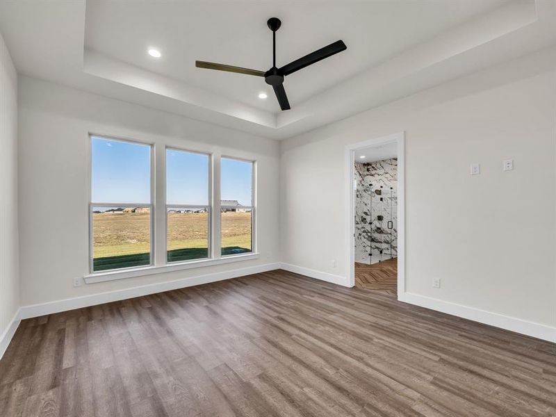 Empty room with ceiling fan, wood-type flooring, and a raised ceiling