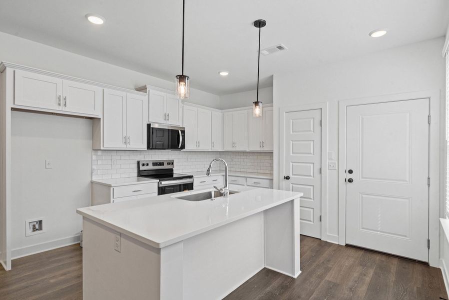 Modern kitchen featuring white cabinetry, subway tile backsplash, stainless steel appliances, a center island with sink, and wood-finish flooring