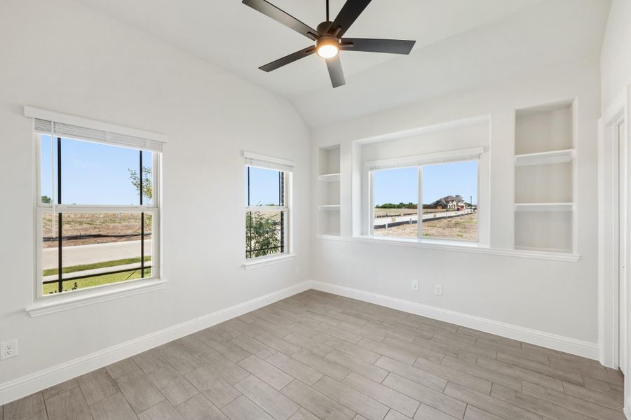 Empty room with vaulted ceiling, ceiling fan, built-in shelves, and wood-look tile floors Empty room with vaulted ceiling, ceiling fan, built-in shelves, and wood-look tile floors