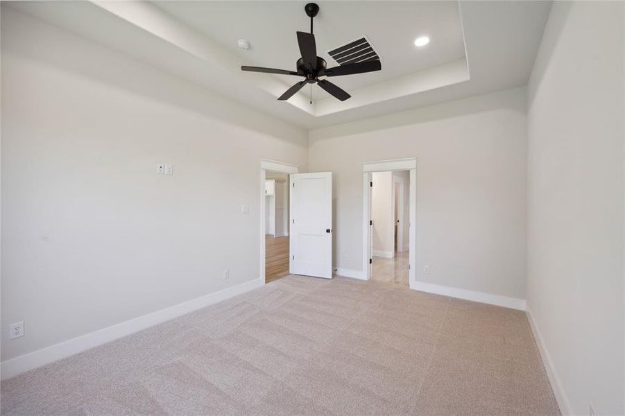 Unfurnished bedroom featuring ceiling fan, light colored carpet, a high ceiling, and a tray ceiling