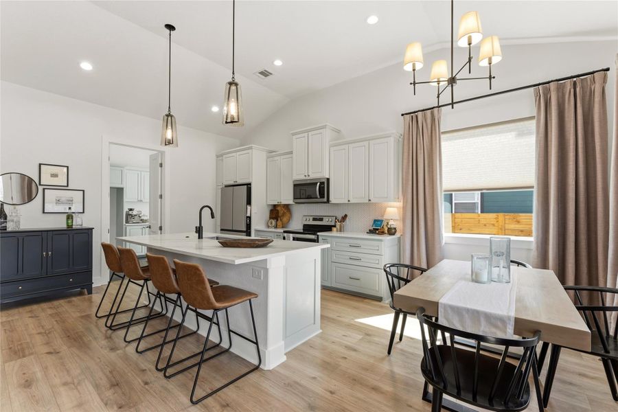 Kitchen with vaulted ceiling, white cabinetry, a kitchen breakfast bar, light wood-style flooring, and a kitchen island with sink
