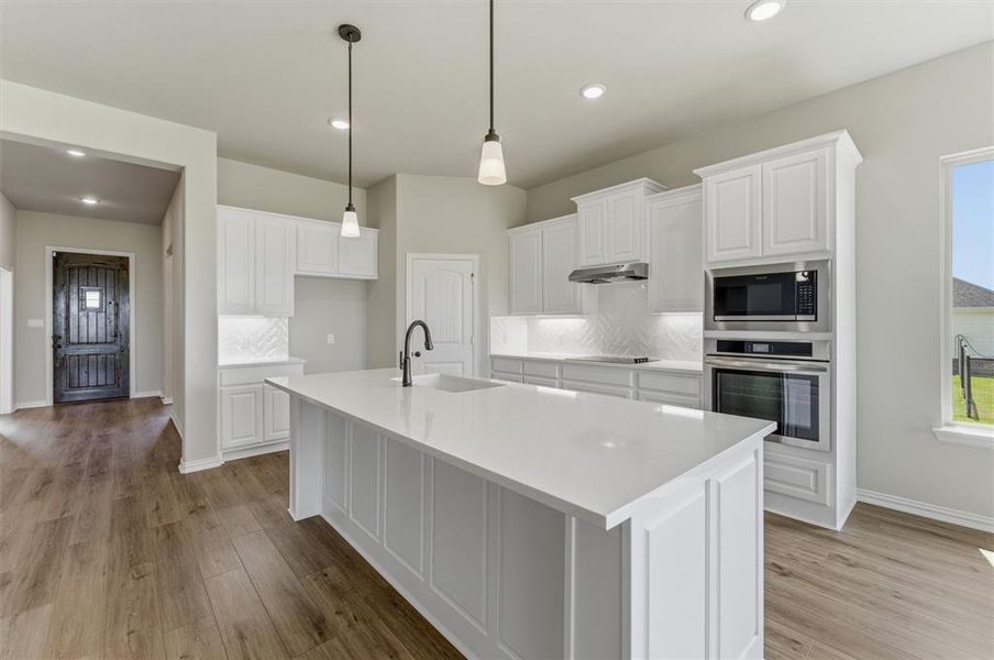 Kitchen with backsplash, stainless steel appliances, white cabinets, a kitchen island with sink, and light wood-type flooring Kitchen with backsplash, stainless steel appliances, white cabinets, a kitchen island with sink, and light wood-type flooring