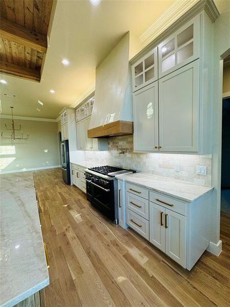 Kitchen with white cabinetry, custom range hood, light hardwood / wood-style floors, and double oven range