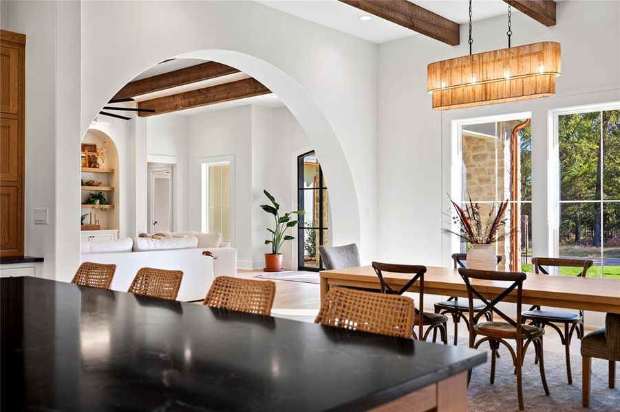 Dining space with beamed ceiling, arched walkways, built in shelves, and wood finished floors