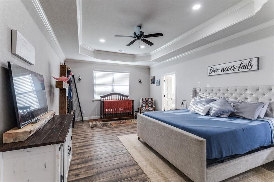 Bedroom featuring crown molding, a raised ceiling, wood finished floors, recessed lighting, and a ceiling fan
