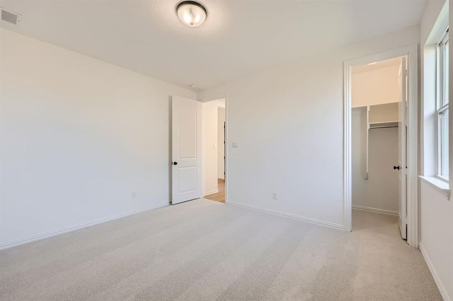 Unfurnished bedroom featuring light carpet, a closet, and a walk in closet