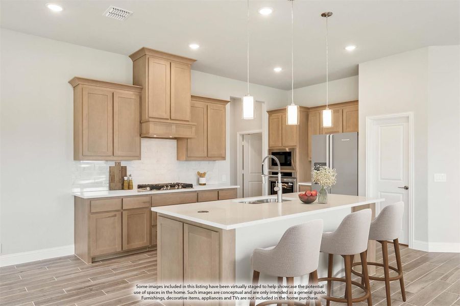 Kitchen with light wood cabinets, large center island with seating, pendant lights, and stainless steel appliances